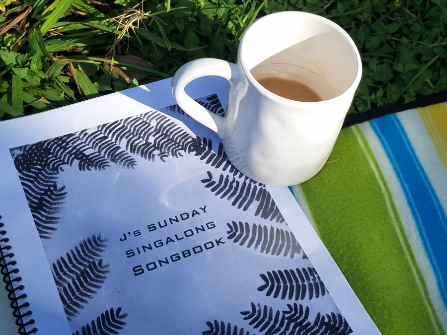 J's Sunday Singalong Songbook w cup of coffee in the sun on the grass